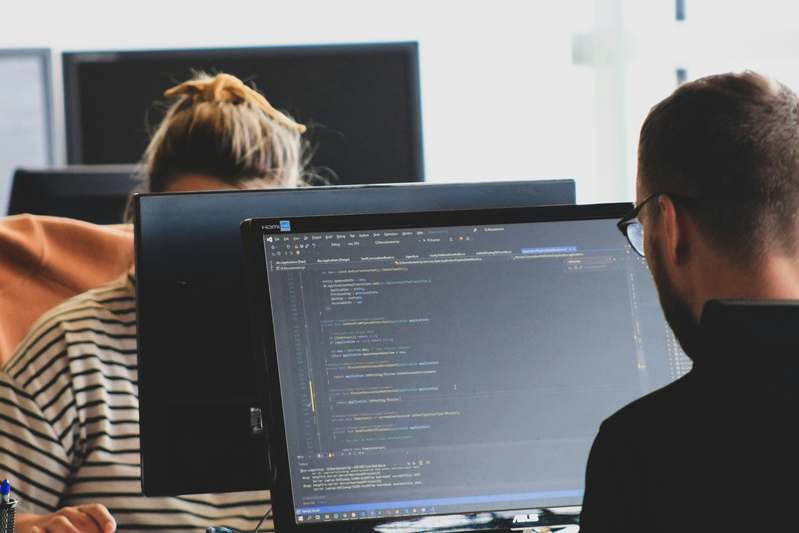 Developer writing C++ game code with dual monitors showing code and game output